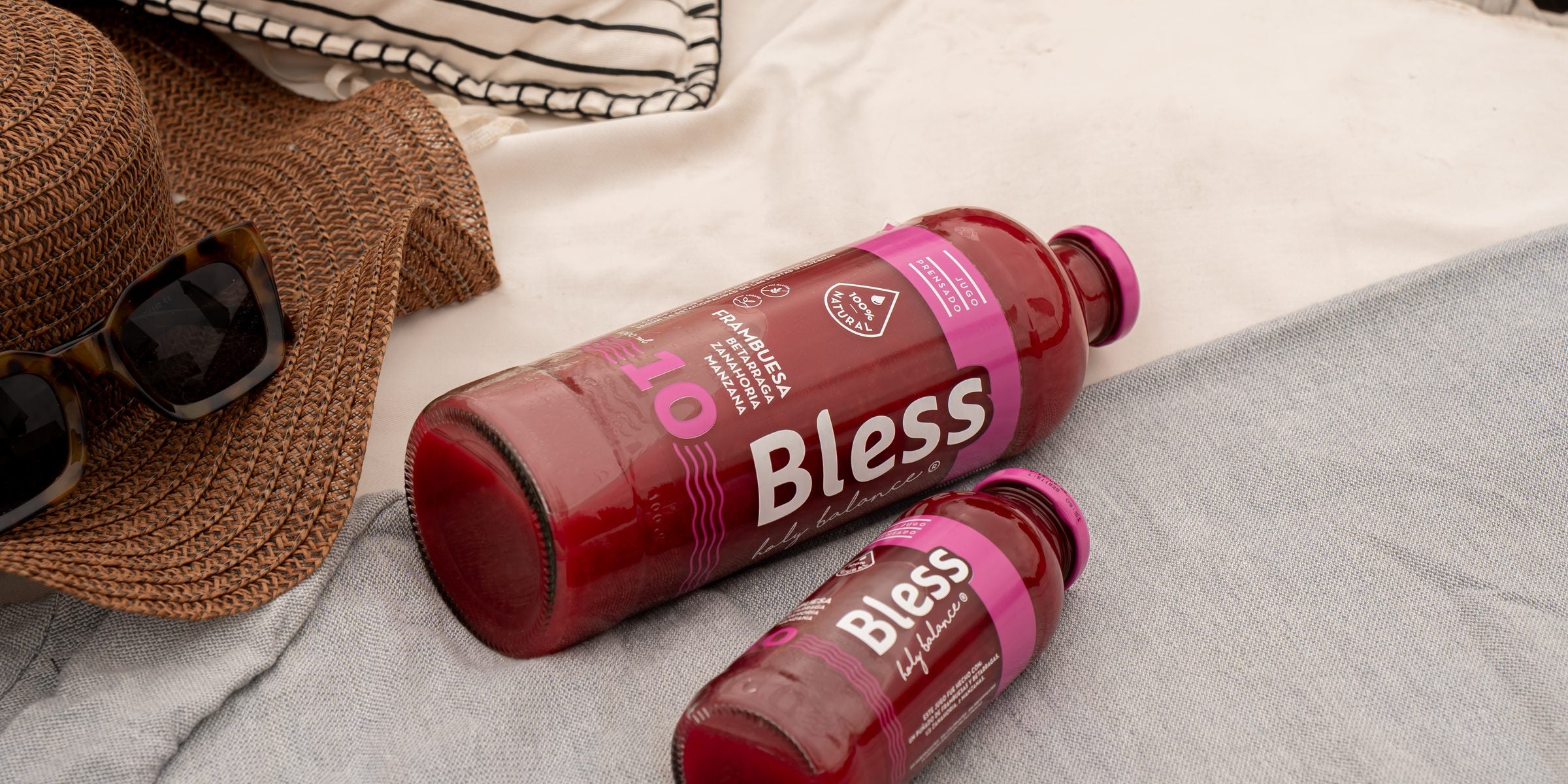 Botellas de jugo Bless sobre una manta, con sombrero y lentes